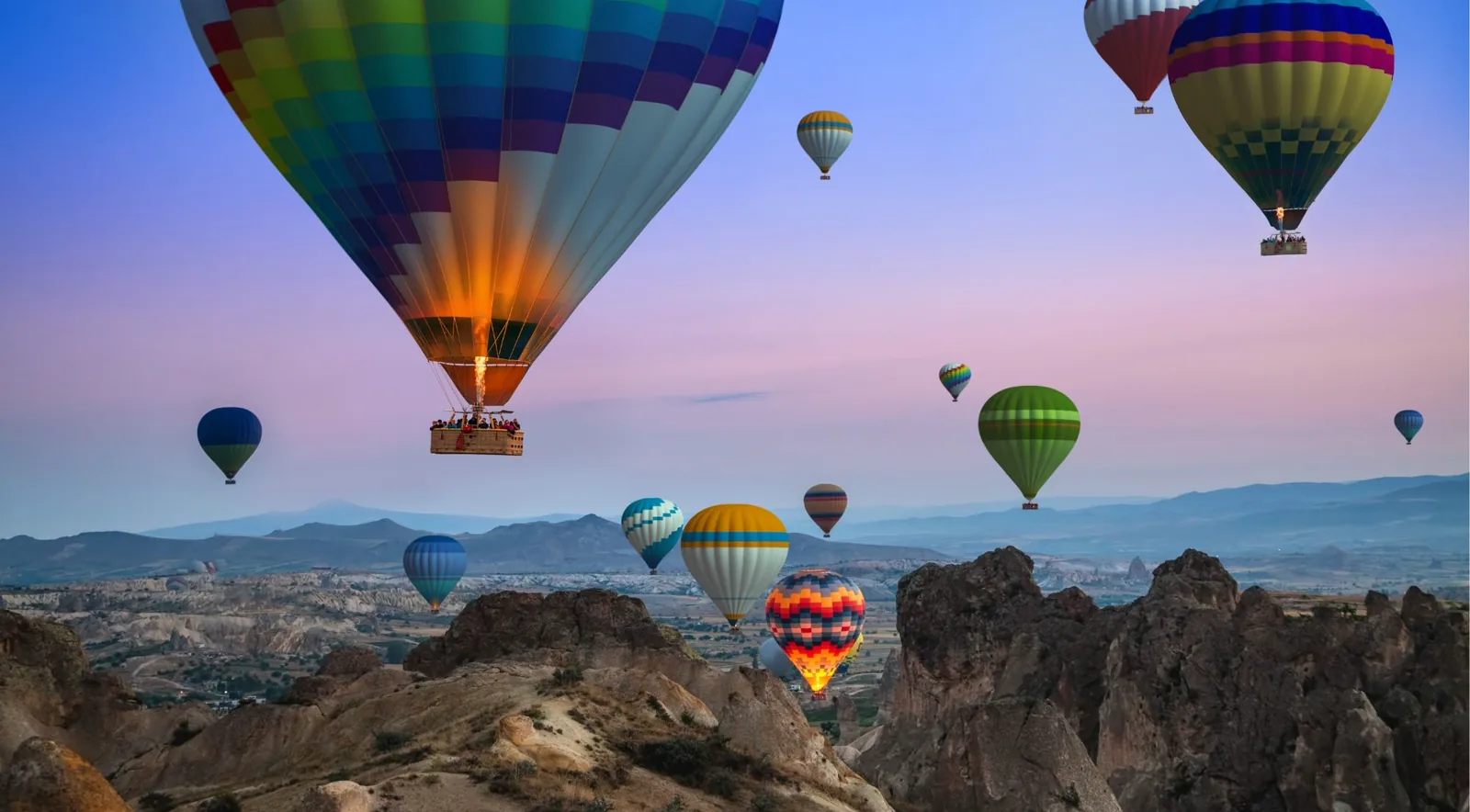 Dozens of balloons rising over Göreme's fairy chimneys in October's peak iconic light